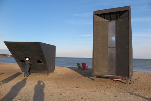 Woodbine Beach: Winter Stations art installation #CemreÖnertürk #EgeÇakır (2022) “Enter Face” designed as two dark boxes, now has two lounge chairs not in the original specification. Shorter east box has three holes where participants can stick their heads in, for a common view of a textured transparent screen while physically isolated. The taller west box textured vertical screen looks inland, with lakeside metal rails despite signs discouraging climbing. (Woodbine Beach, Toronto, Ontario) 20200306